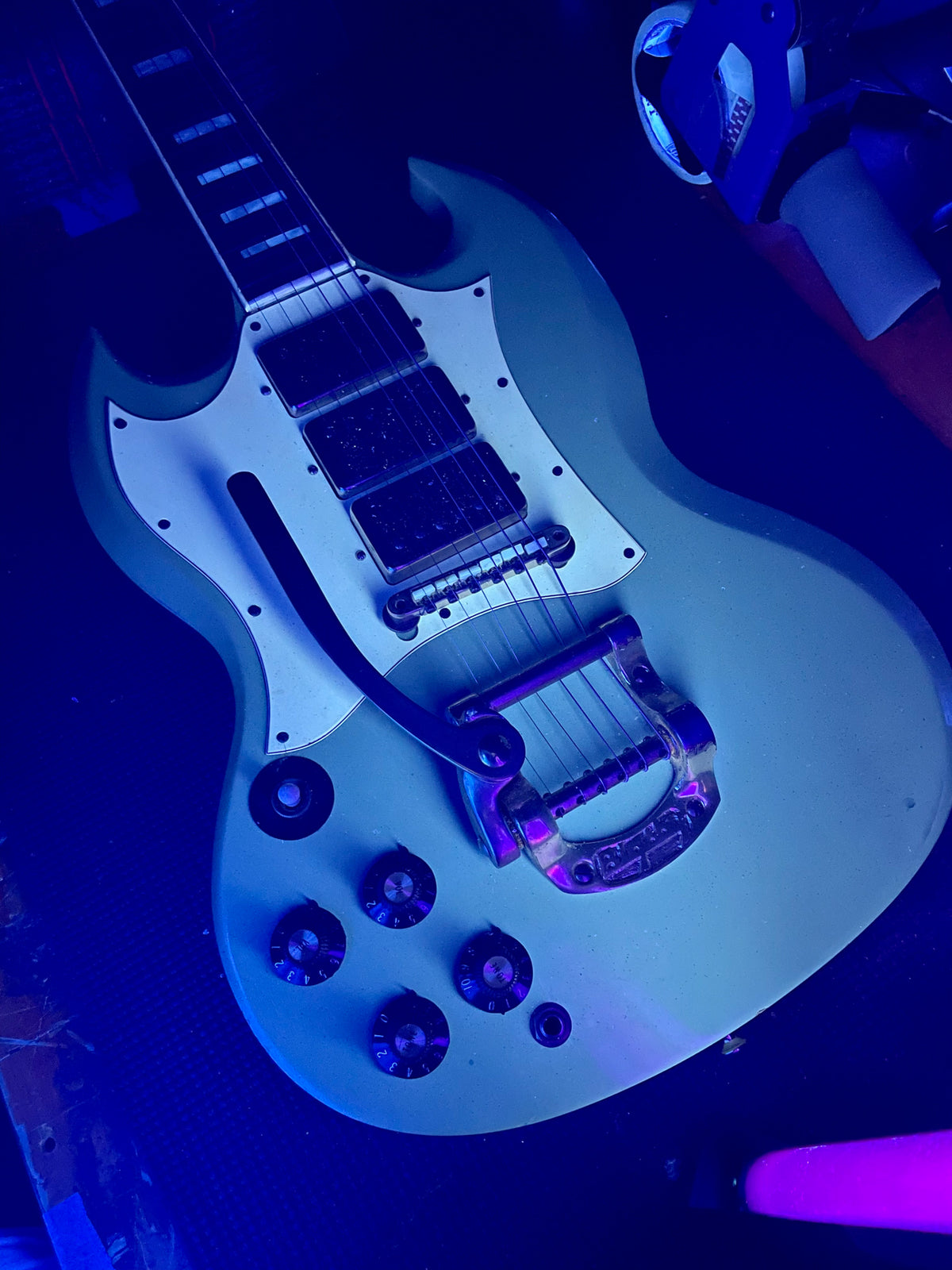 Pelham Blue SG body, angled from the neck, shows three humbuckers, a Bigsby vibrato, and four black control knobs.