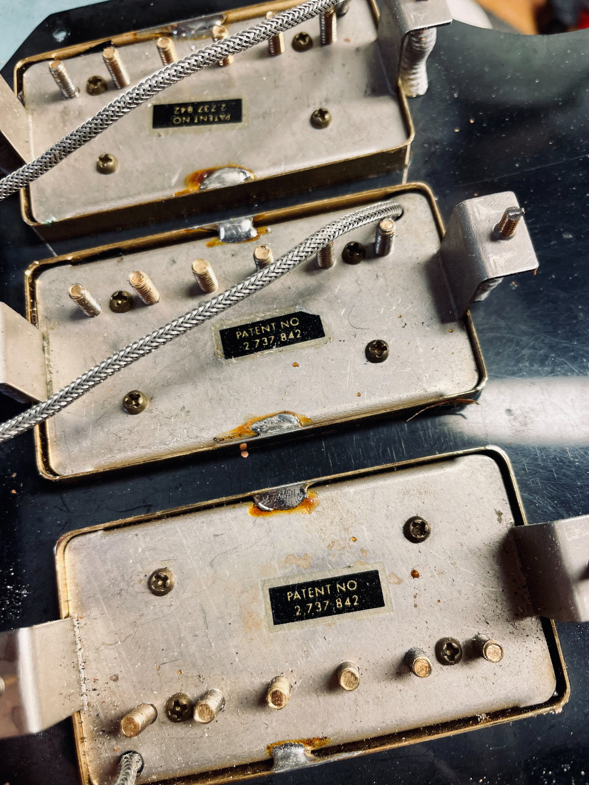 Close-up of three tarnished silver-colored humbucker pickups with exposed gold pole pieces and braided wire.