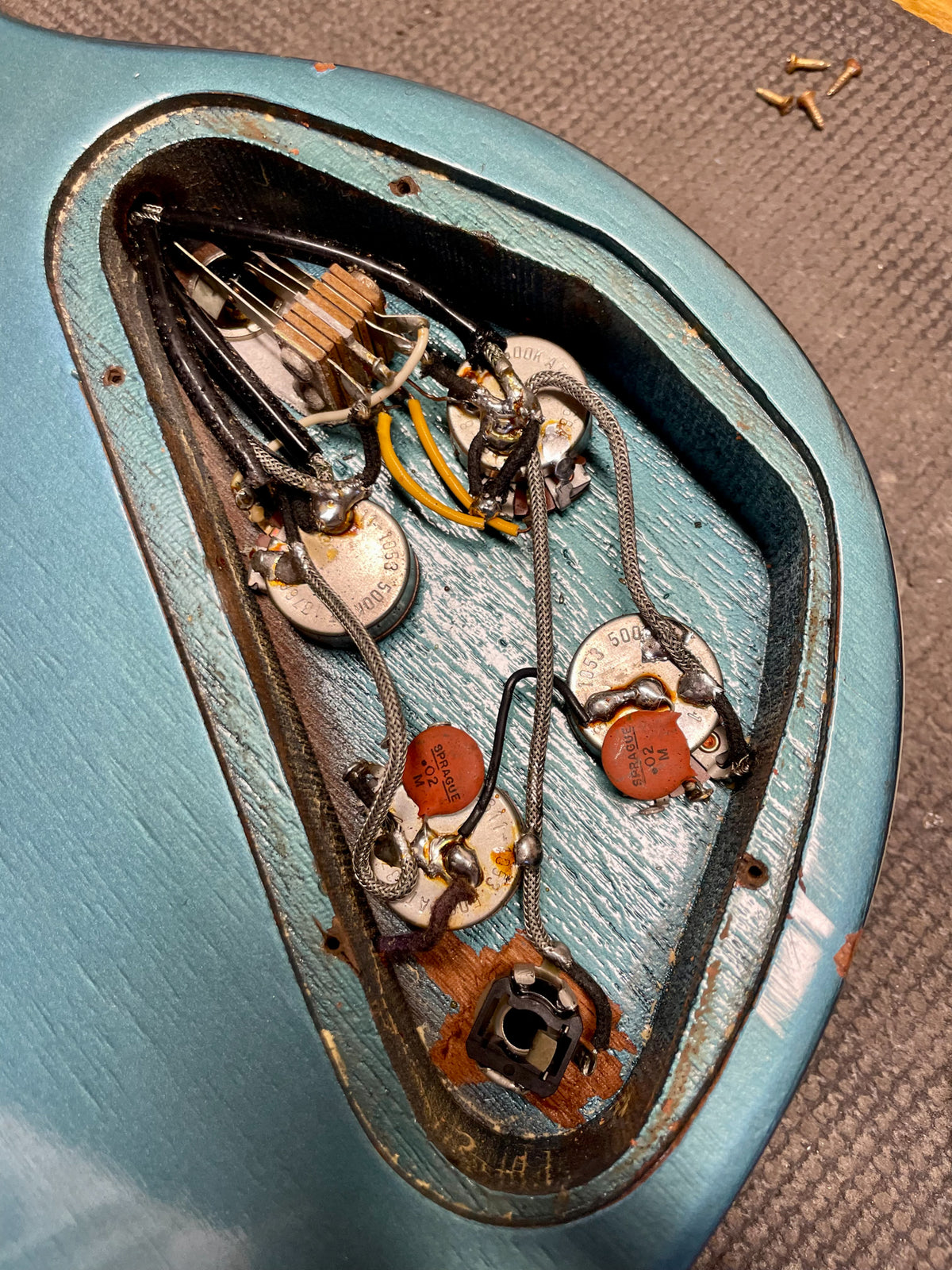 Close-up of the guitar's control cavity, revealing four pots, two orange capacitors, and wiring against the Pelham Blue finish.