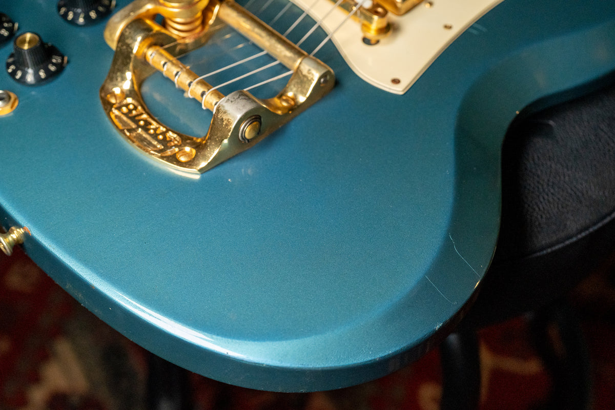 Close-up of the Pelham Blue body, showing the gold Bigsby vibrato, cream pickguard, and finish checking near the lower bout.