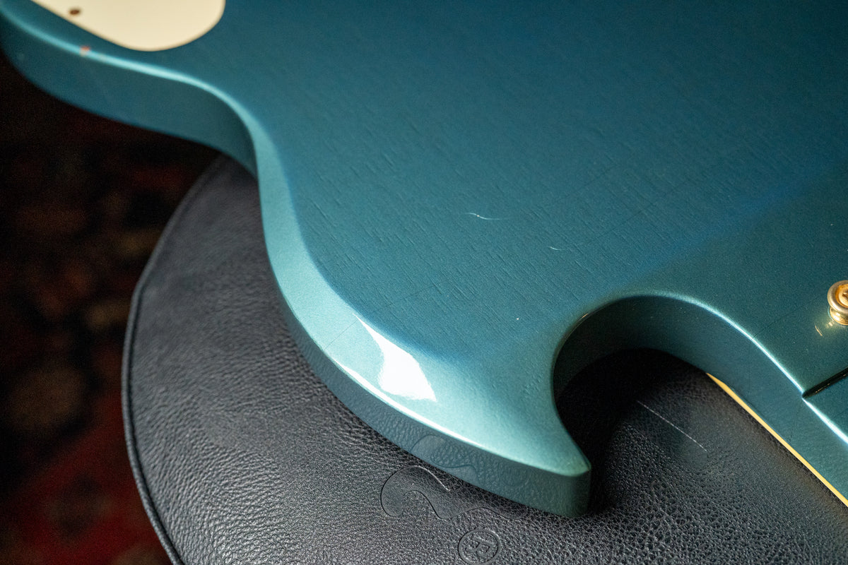 Close-up of the guitar's lower body, showing the Pelham Blue finish with visible checking and light scratches, resting on a black leather surface.