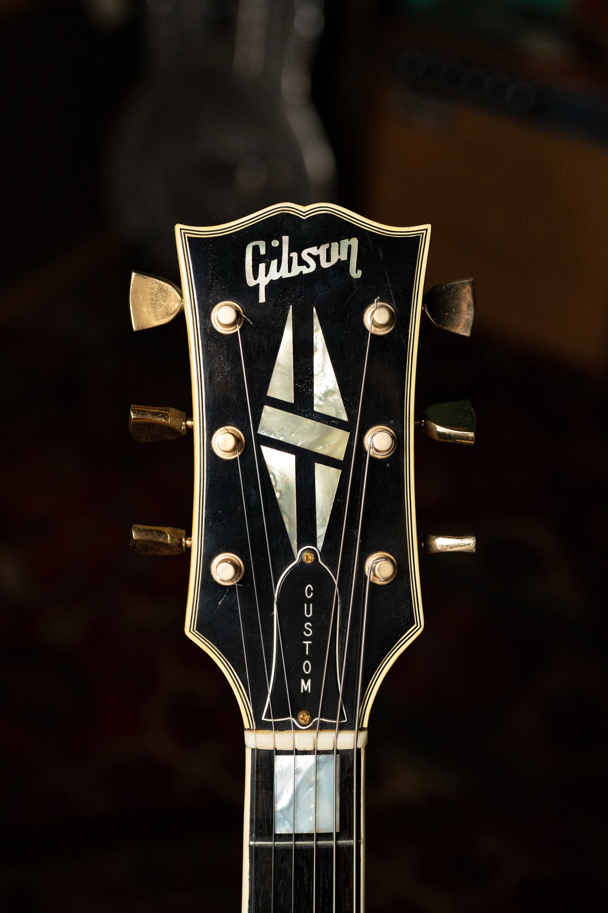 Close-up of the black headstock with mother-of-pearl inlays, gold tuners, and visible finish checking.