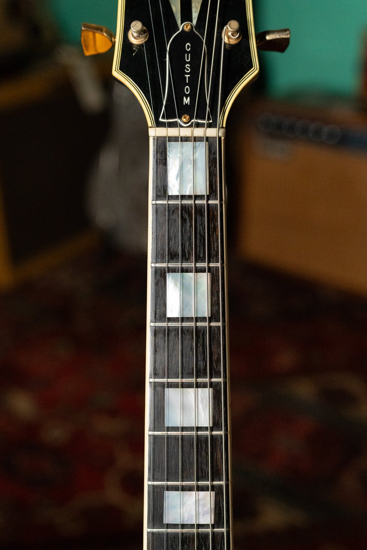Close-up of the guitar's headstock and upper fretboard, showing gold tuners, mother-of-pearl block inlays, and binding.