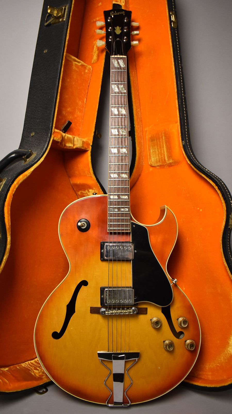 Full-length, front view of a cherry sunburst hollow-body electric guitar with two humbuckers, in an open, orange-lined hard case.