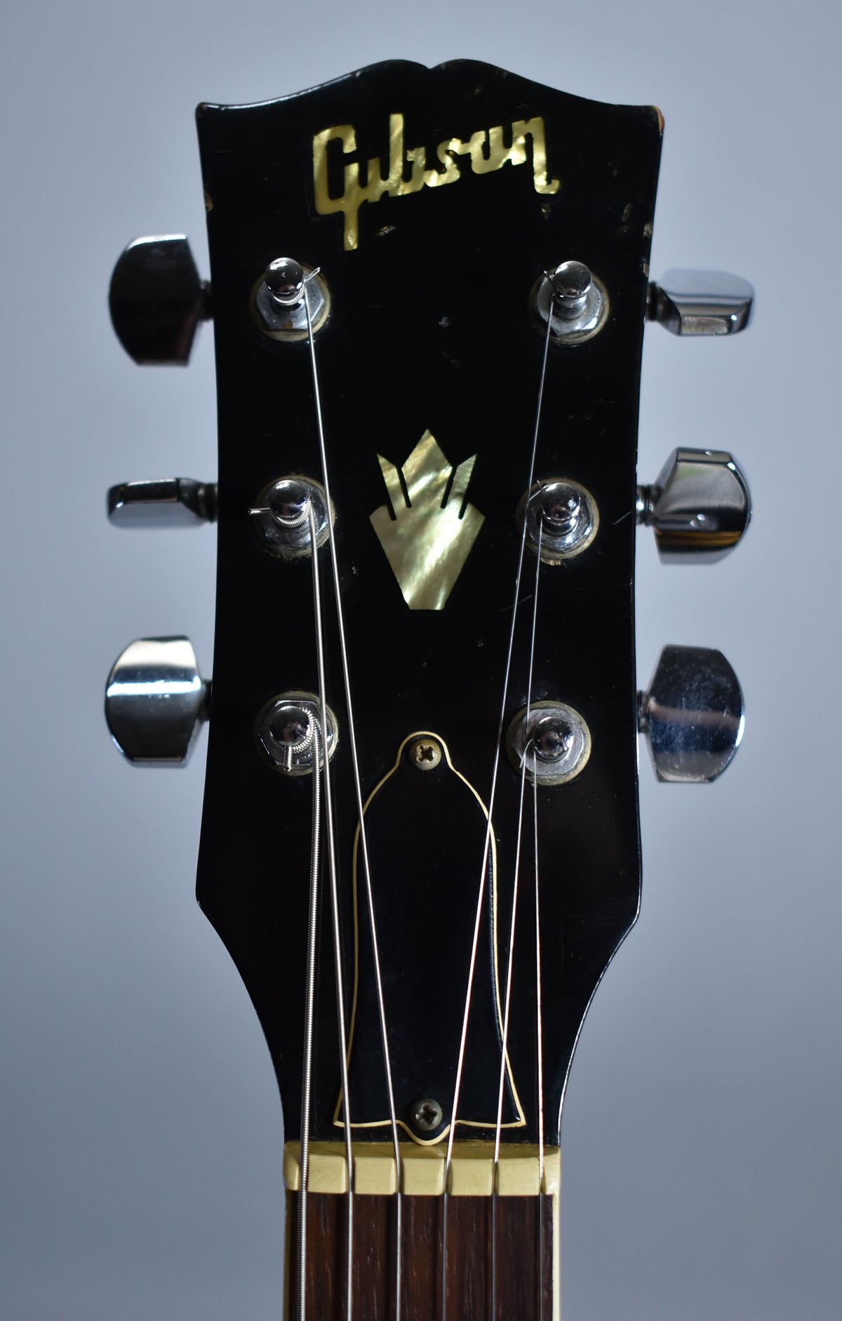 Close-up of the black headstock with gold logo, mother-of-pearl crown inlay, six chrome tuners, and visible finish wear.