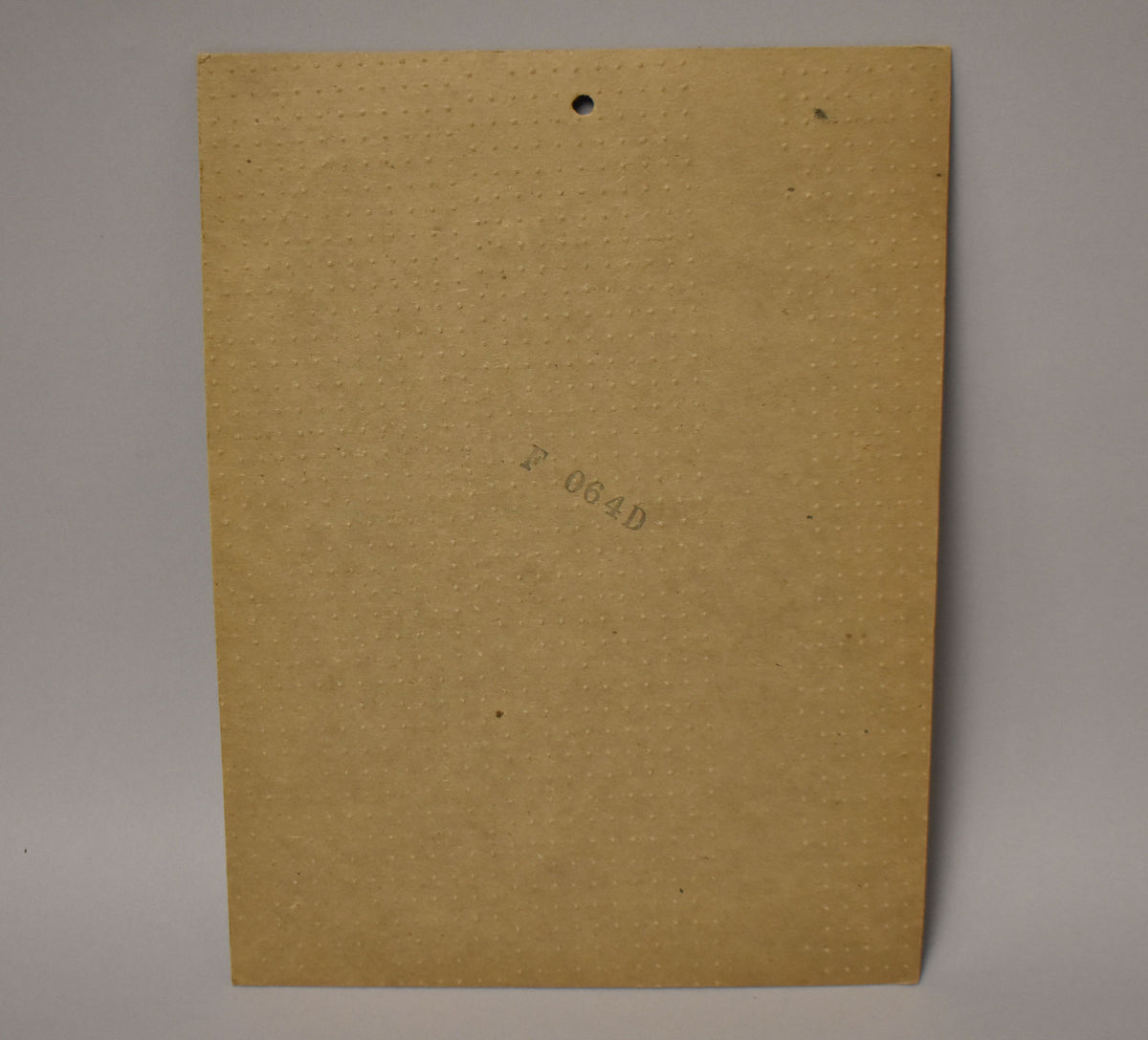 The back of the black anodized pickguard is covered in a textured, light brown paper backing with a small hole at the top.