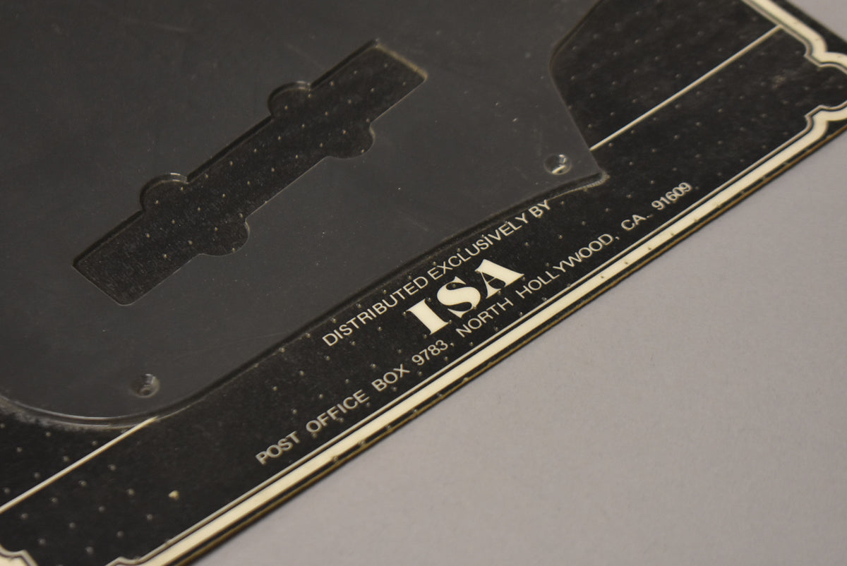 Close-up of the black anodized pickguard's back, revealing a clear plastic cover over the pickup route and white text on a black sticker.