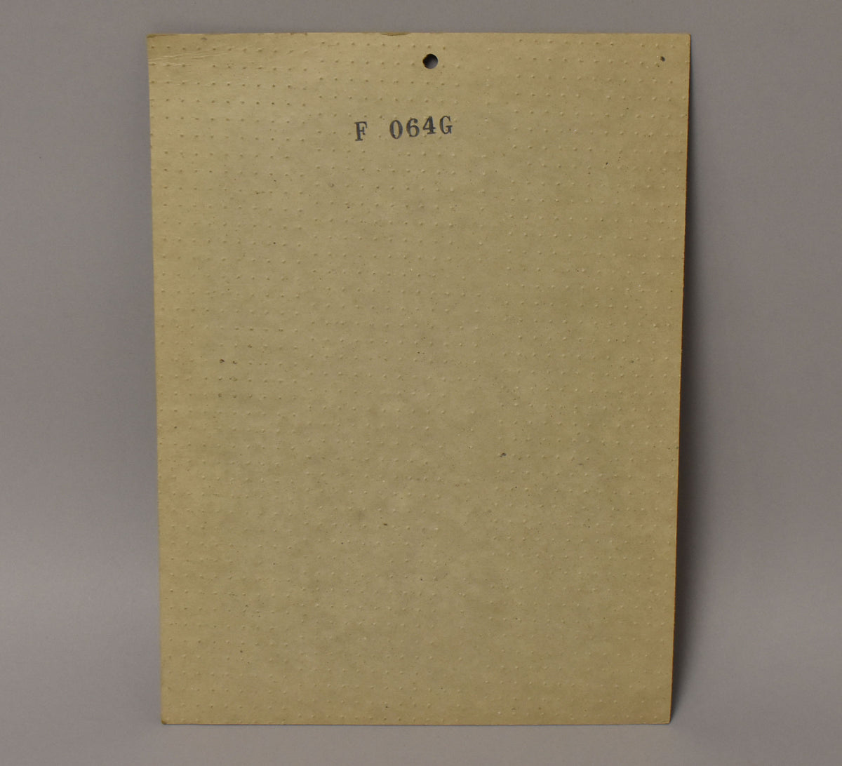 The back of the white pickguard, showing a textured tan surface with a punched hole and "F 064G" stamped near the top.
