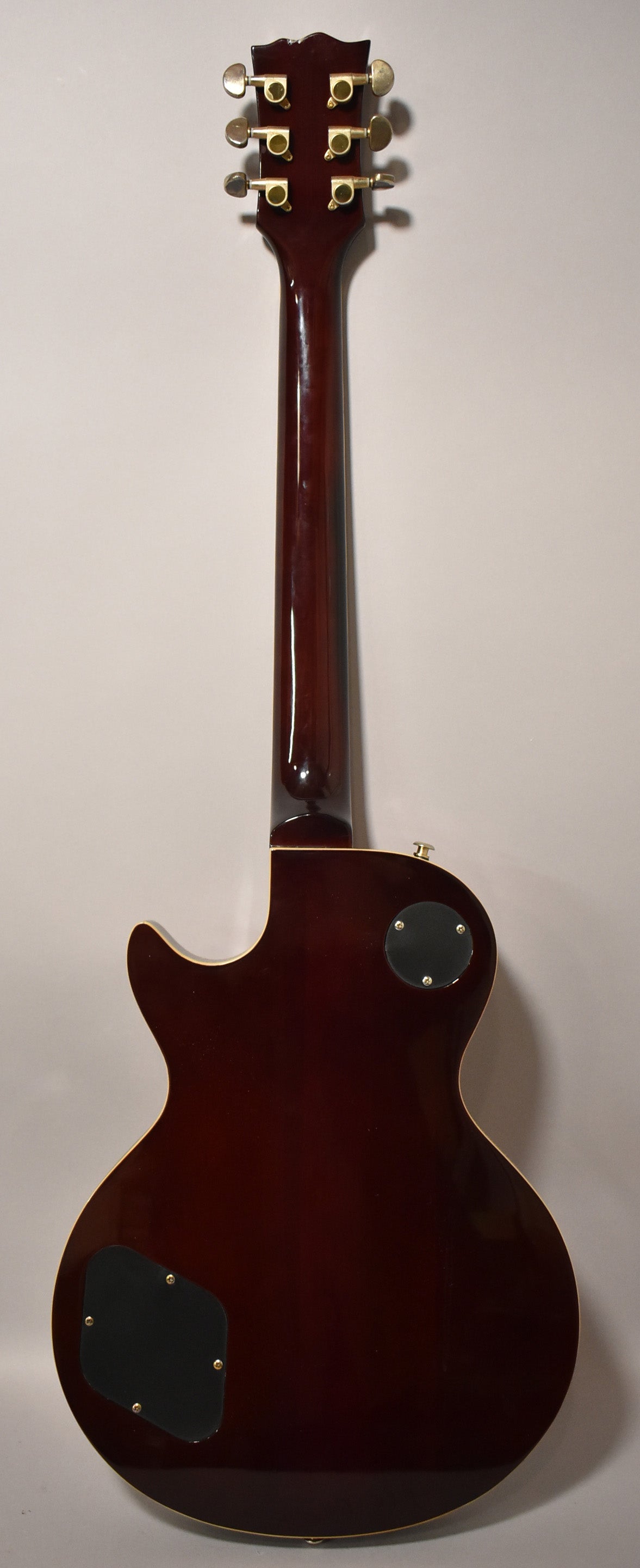 Full rear view of a dark cherry sunburst electric guitar with gold tuners, two black control cavity covers, and light binding.