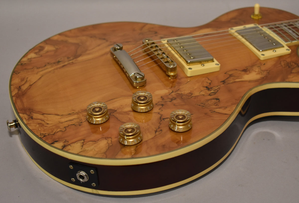 Close-up of the guitar's lower bout, showing the natural burl top, four gold speed knobs, cream pickup rings, and dark brown sides.