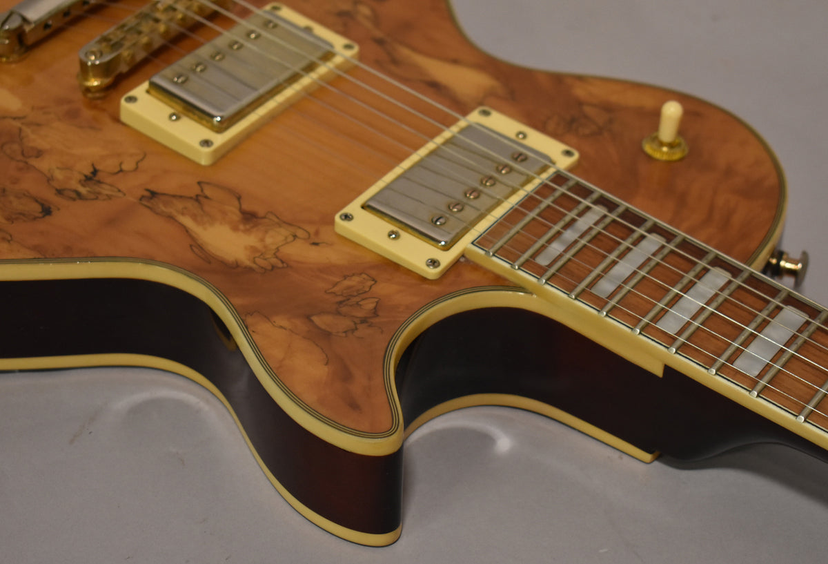 Close-up of the guitar's natural burl top, showing cream humbucker rings, trapezoid inlays, and dark brown sides with cream binding.