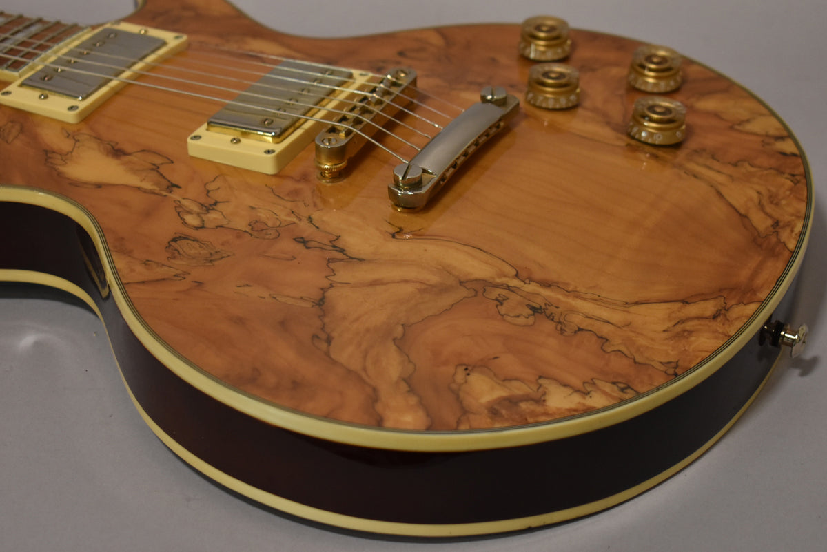 Close-up of the guitar's body, showing the natural burl wood finish, cream pickup rings, gold hardware, and four gold control knobs.