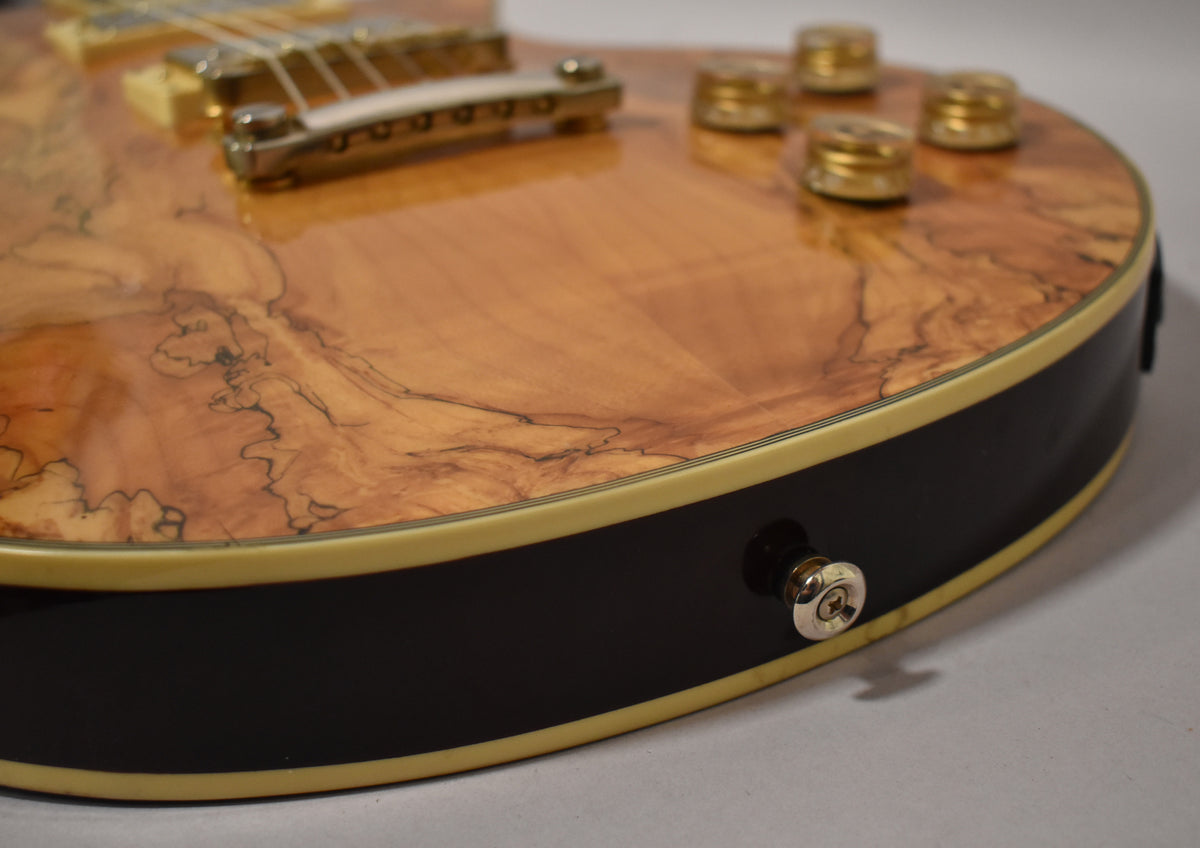 Close-up of the guitar's lower bout, showing the natural spalted maple top, black sides, cream binding, and chrome output jack.