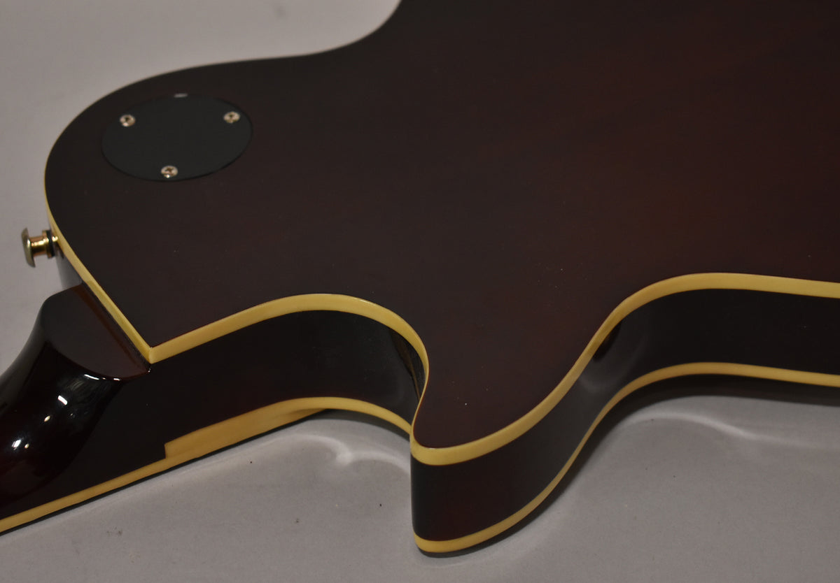 The guitar's dark brown back is visible, with cream binding along the edges and a black control cavity cover near the strap button.
