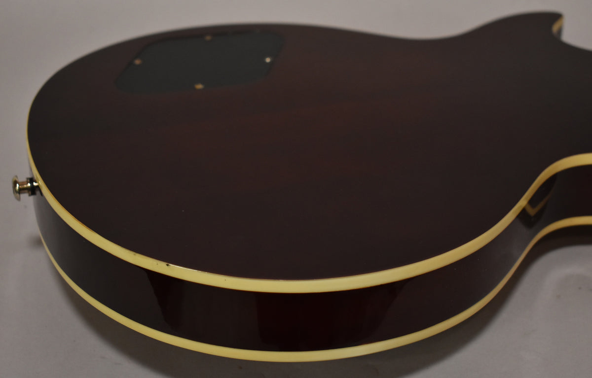 The guitar's dark brown back and side are visible, with cream binding and a black control cavity cover.