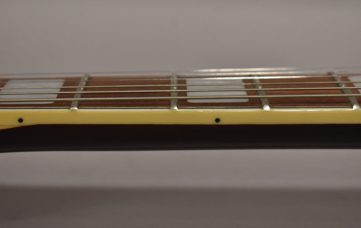 Close-up of the guitar's fretboard, showing dark wood, rectangular pearloid inlays, and cream binding with black side dots.