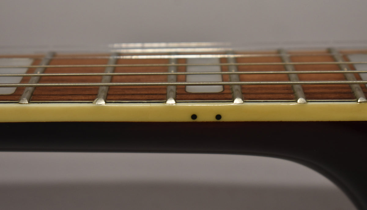 Close-up of the guitar's fretboard from the side, showing dark wood, metal frets, cream binding, and two black side dot markers.