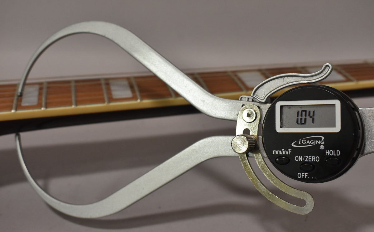 A digital caliper measures the fret height on the guitar's rosewood fretboard with rectangular pearloid inlays.