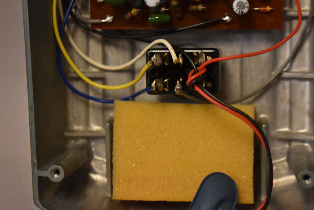 An overhead view of the pedal's open aluminum casing, showing internal wiring, a circuit board, and a yellow foam block.