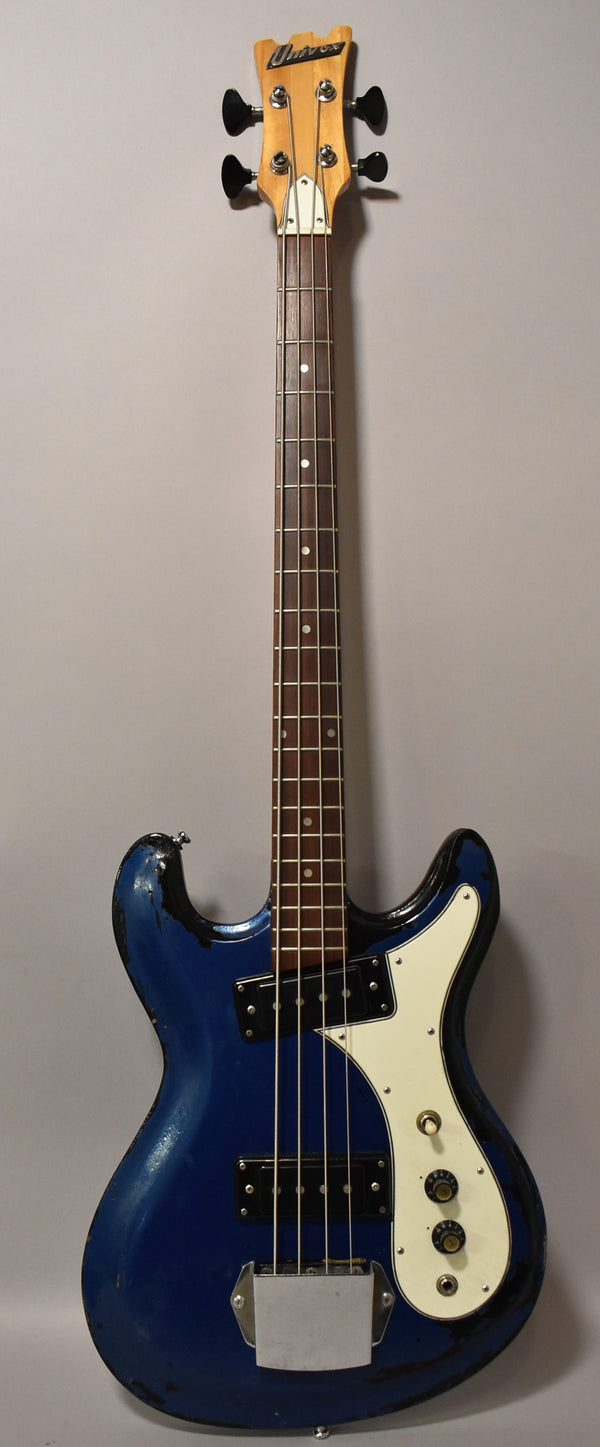 Full-length view of a metallic blue bass with heavy wear, a white pickguard, two black pickups, and a chrome bridge cover.