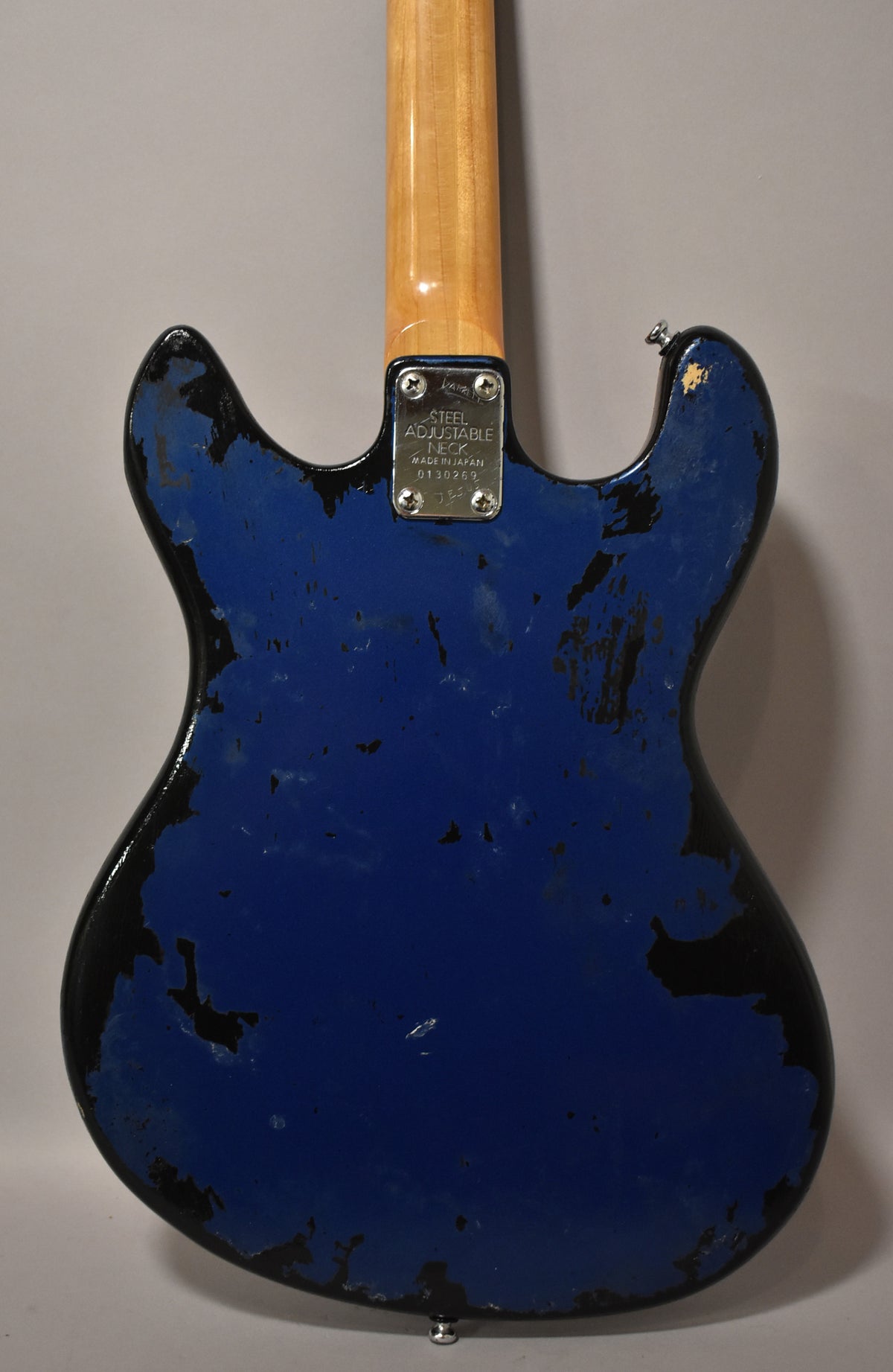 Rear view of a metallic blue bass with heavy paint chipping revealing black undercoat, a maple neck, and a chrome neck plate.