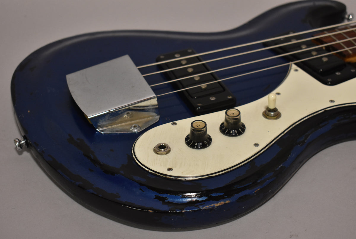 The metallic blue bass body, with heavy paint chipping revealing black undercoat, features a chrome bridge cover and white pickguard.