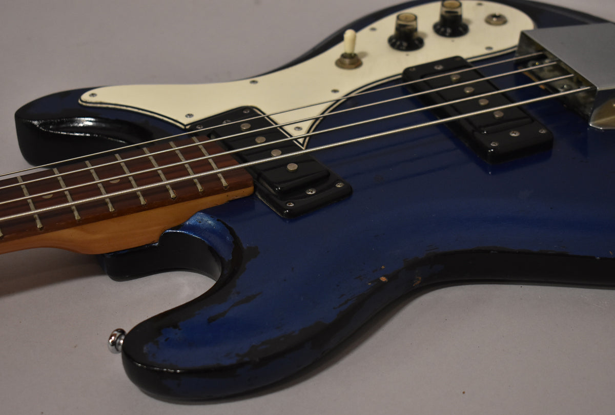 Close-up of the metallic blue bass body, showing heavy wear and chipping on the edges, cream pickguard, and two black control knobs.