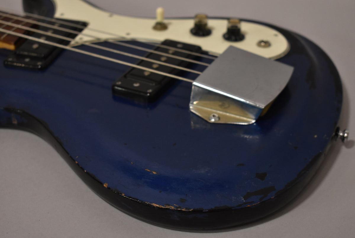 Close-up of the bass body, showing the metallic blue finish with significant wear, a chrome bridge cover, and two black pickups.