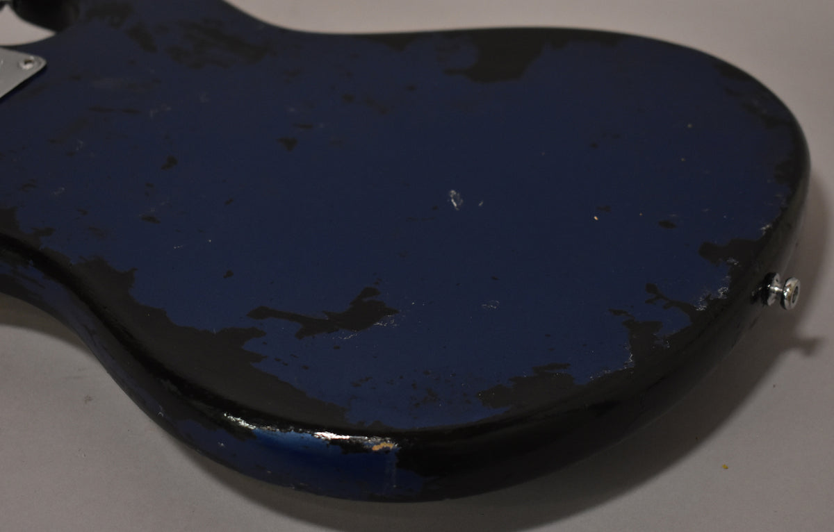The bass body's metallic blue finish is heavily chipped and worn, revealing black undercoat, with a chrome strap button visible on the lower bout.