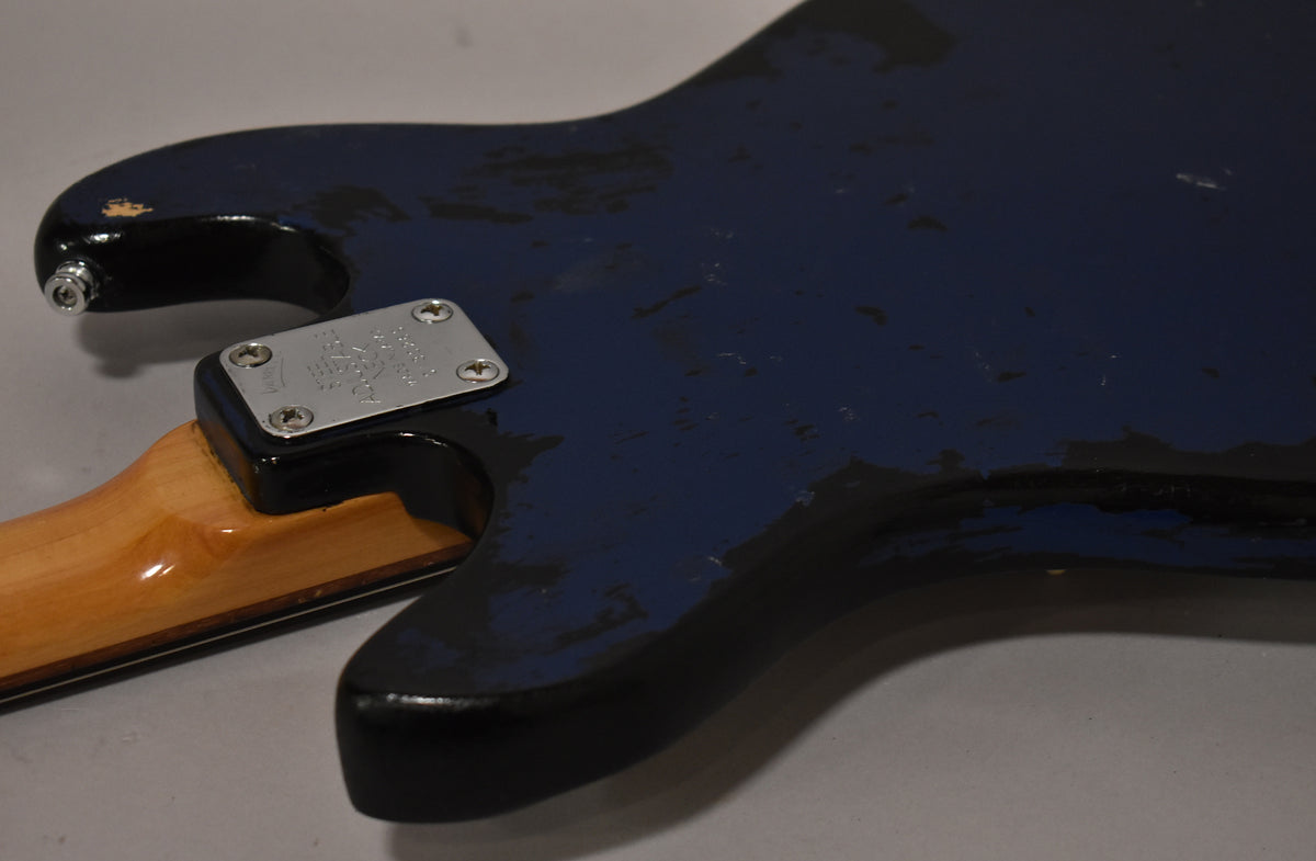 Close-up of the bass's back, showing the metallic blue finish with heavy wear revealing black and wood beneath, and the neck plate.