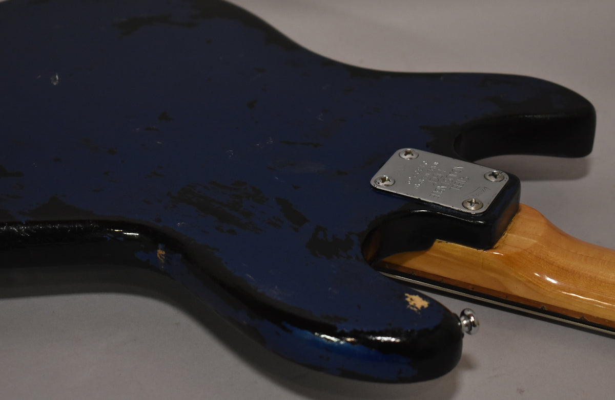 Angled close-up of the bass's lower body, showing heavy wear on the metallic blue finish, revealing black and natural wood beneath.