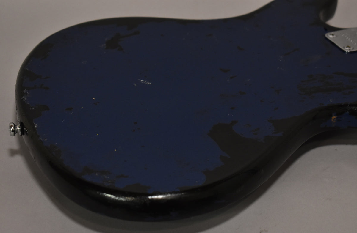 The metallic blue bass body, viewed from the back, shows extensive wear with large chips and scratches revealing the dark undercoat.