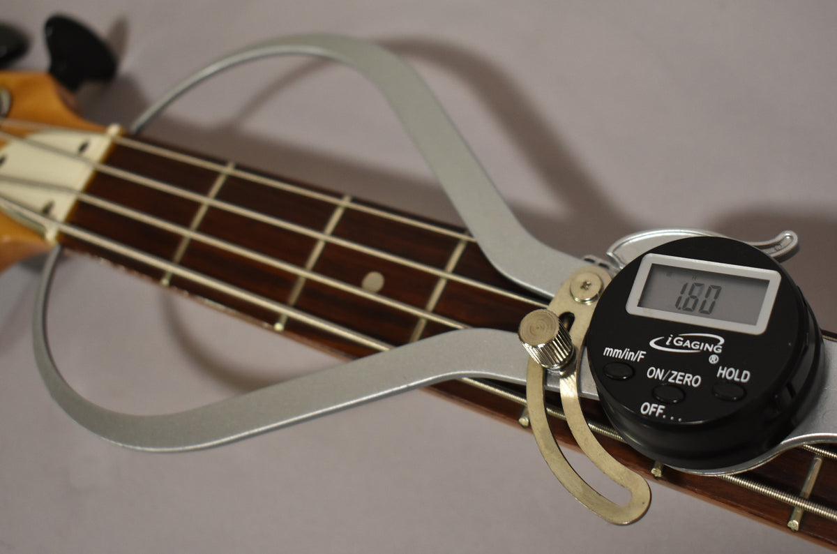 A digital fret rocker tool rests on the bass fretboard, showing a 1.80mm reading, with the headstock visible at the top left.