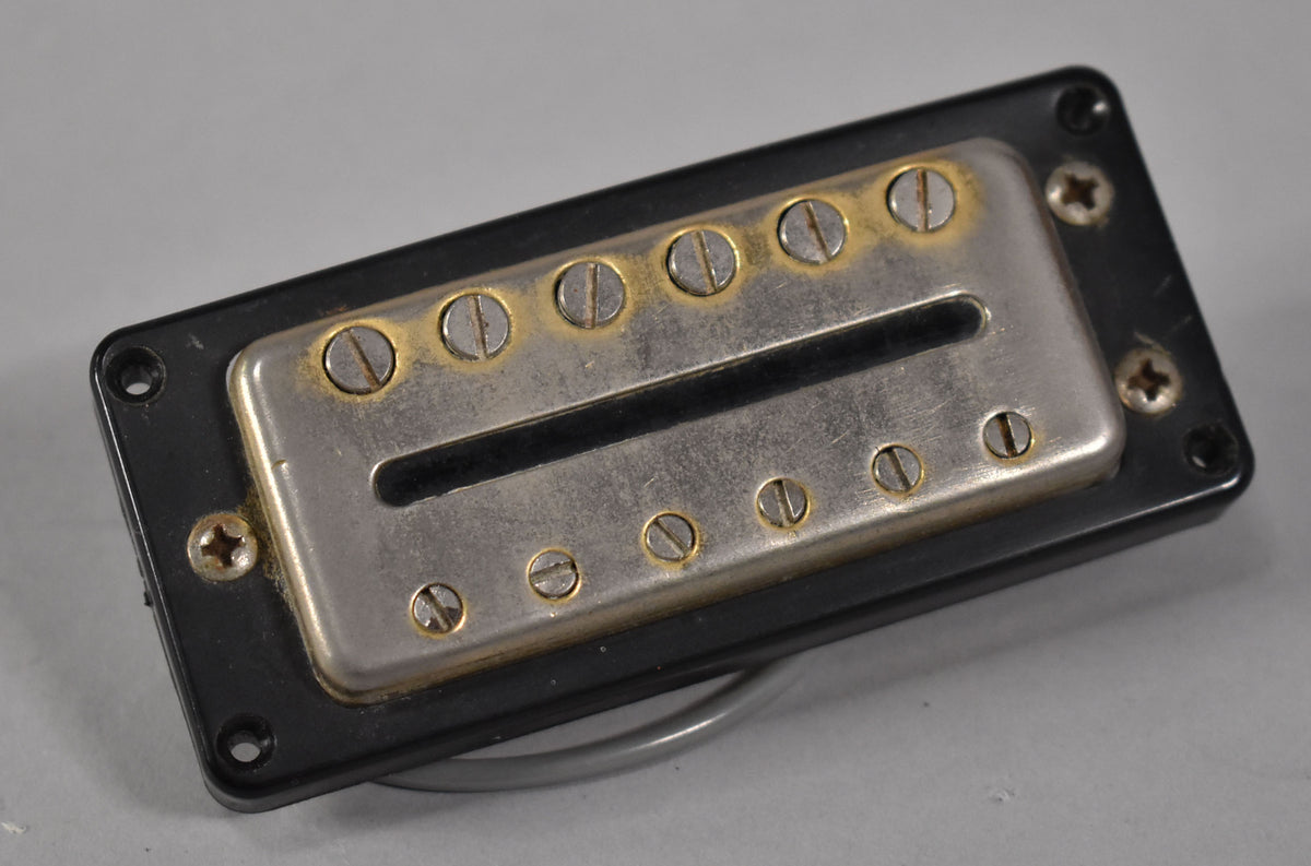 A black humbucker pickup with a tarnished chrome cover and gold-rimmed pole pieces, viewed from a slight angle.