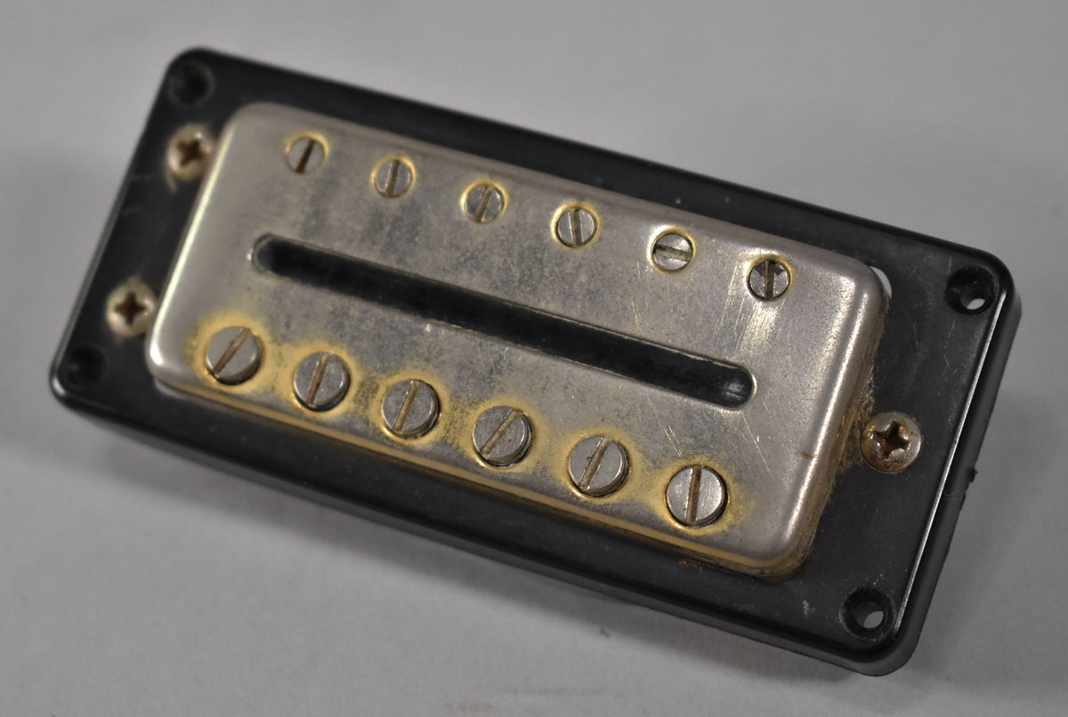A black pickup with a tarnished silver cover and exposed pole pieces, viewed from a slight angle, showing rust around the screws.