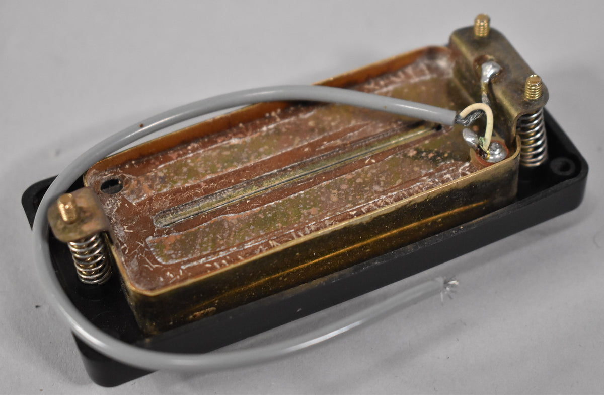 Top-down view of a black pickup with a tarnished brass base, showing exposed wiring and mounting springs.