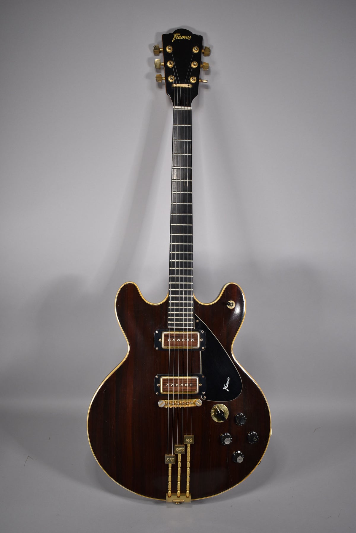 Full-front view of a dark brown semi-hollow electric guitar with gold hardware, two humbuckers, and a multi-switch control panel.