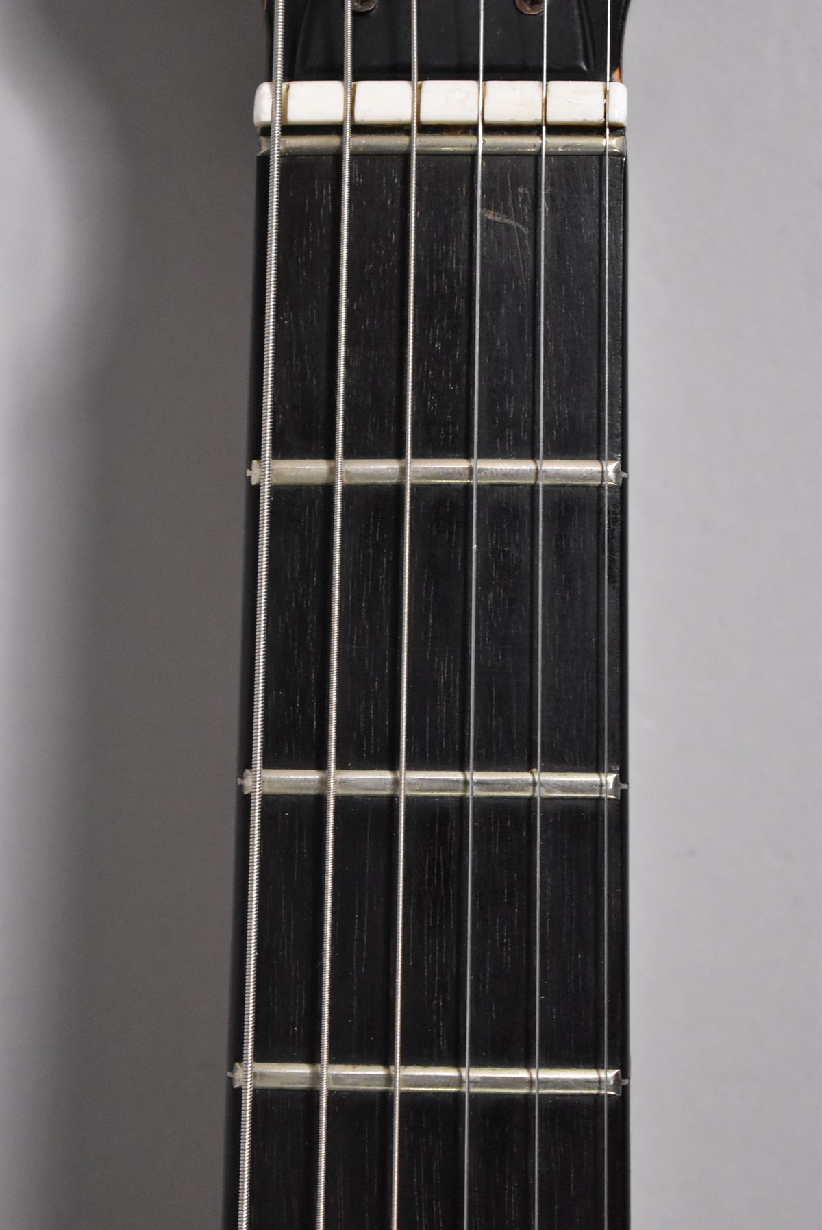 Close-up of the guitar's dark fretboard and six strings, showing a white nut and some light wear on the first few frets.