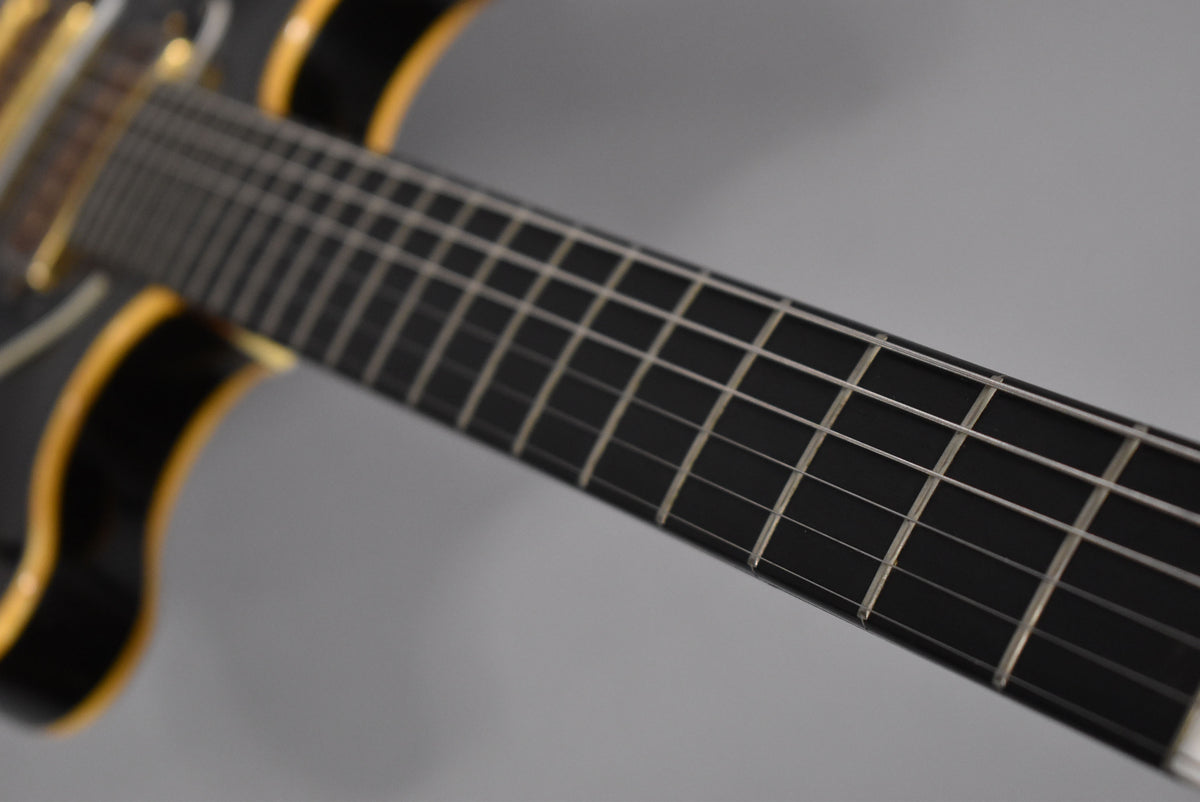 Close-up of the guitar's dark fretboard and frets, with a hint of the glossy black body and yellow binding on the left.