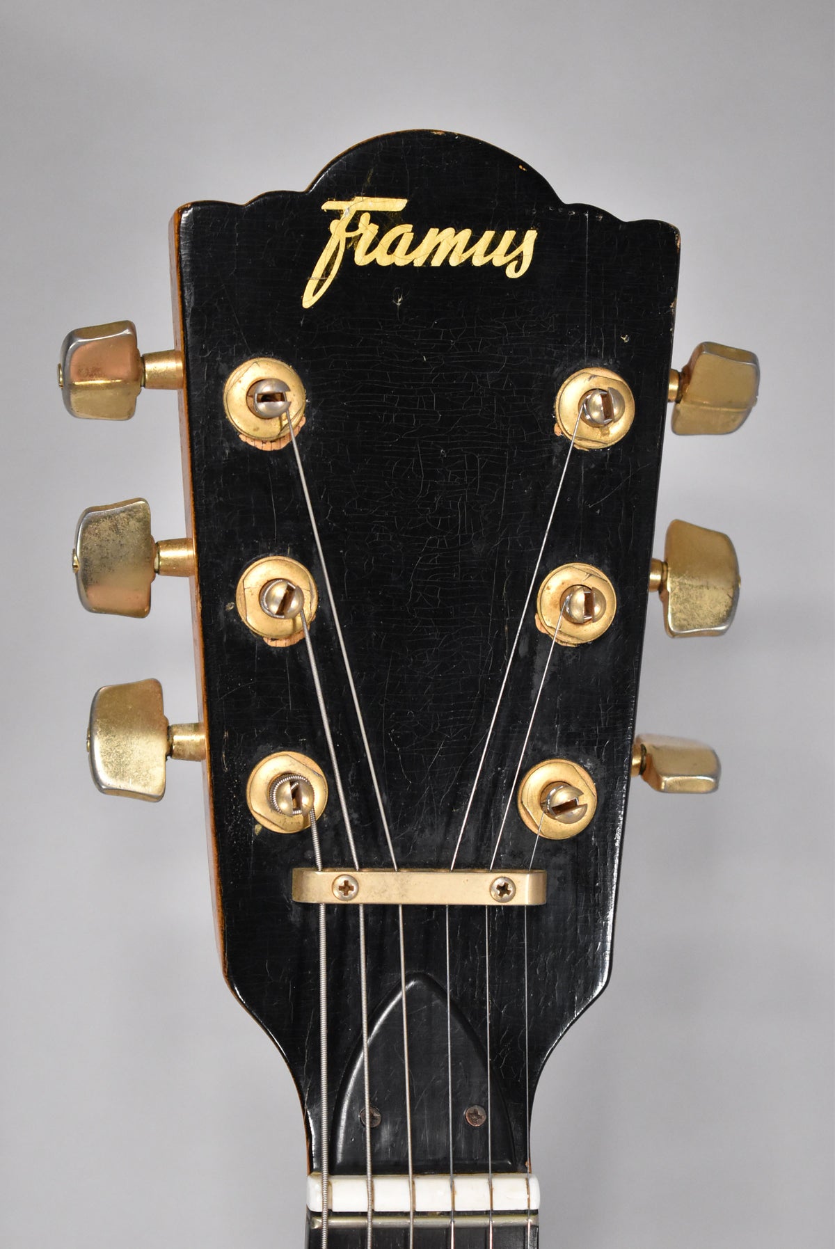 Close-up of the guitar's headstock, showing a black finish with heavy checking, six gold-toned tuners, and a gold string tree.