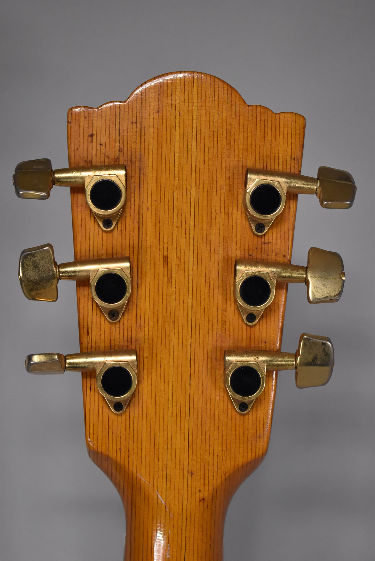 Rear view of the guitar's headstock and neck, showing six gold-toned tuners with black centers and visible wear on the hardware.