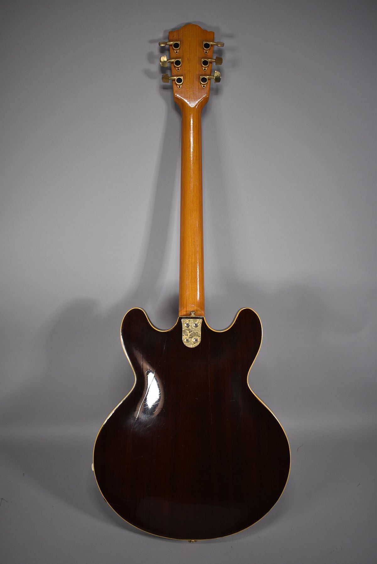 The guitar's dark walnut-finished back shows light wear, with a light-colored neck and gold tuners and neck plate.