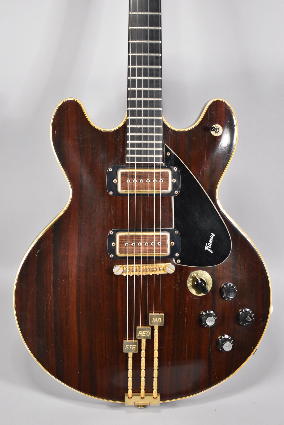 Close-up of a dark walnut hollow-body guitar with gold hardware, two humbuckers, a black pickguard, and visible finish wear.