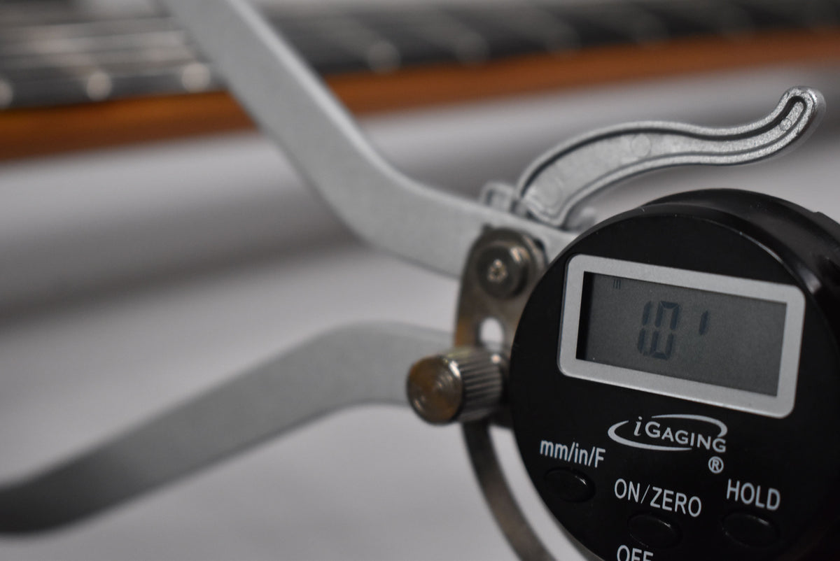 Close-up of the guitar's fretboard and neck, with a digital caliper measuring the fret height at 1.01 inches.
