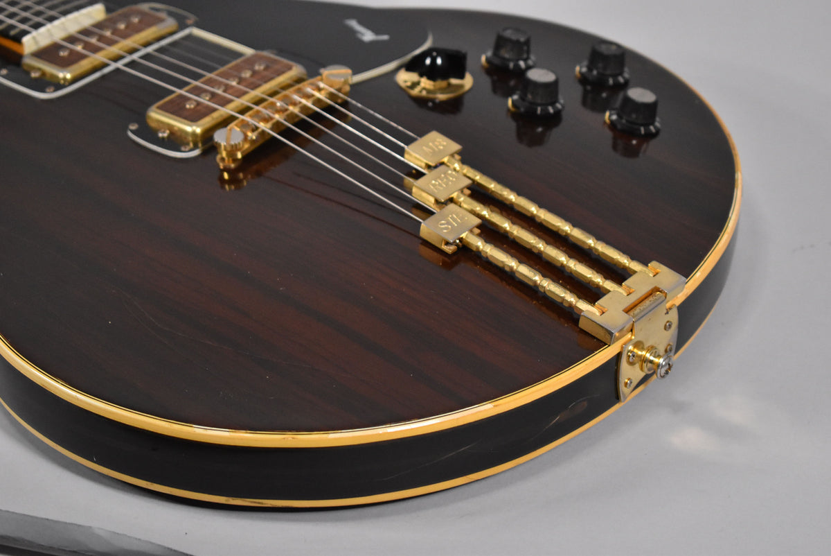 Close-up of the dark walnut body with visible grain, showing gold hardware, four black control knobs, and light binding with some wear.