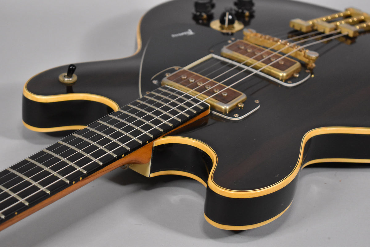 The dark walnut finish electric guitar is angled, showing its fretboard, gold hardware, and cream binding with some visible wear.