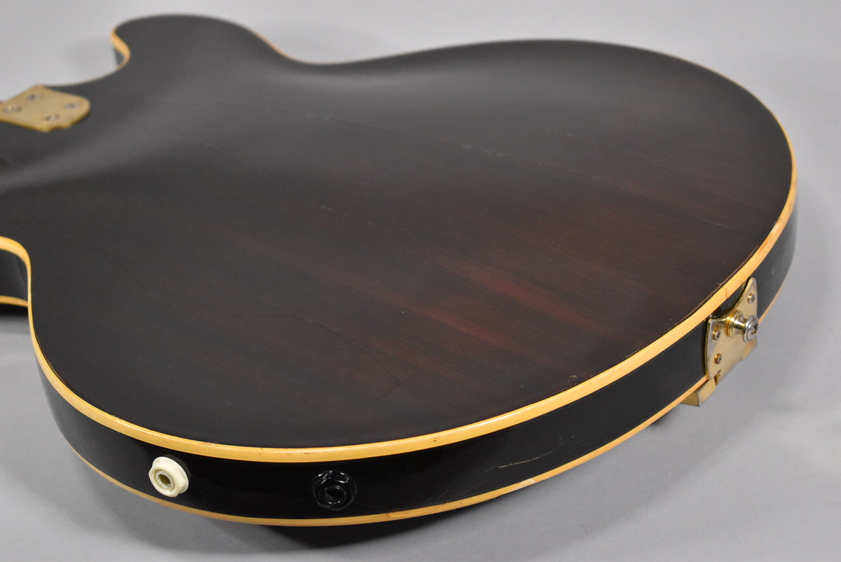 The guitar's dark walnut back and side are visible, with two output jacks, one white and one black, and a gold strap button.