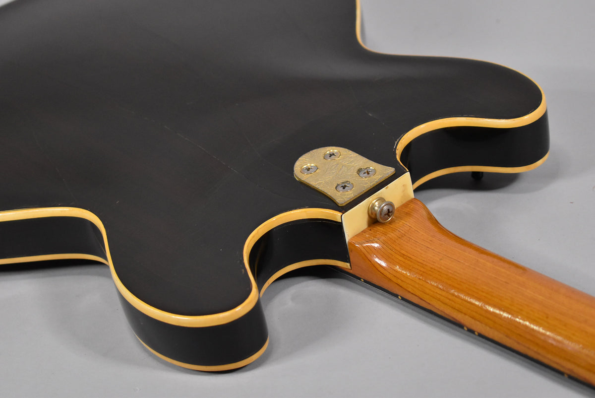 The guitar's black body with cream binding and visible wear on the finish, showing the neck joint and light wood neck.