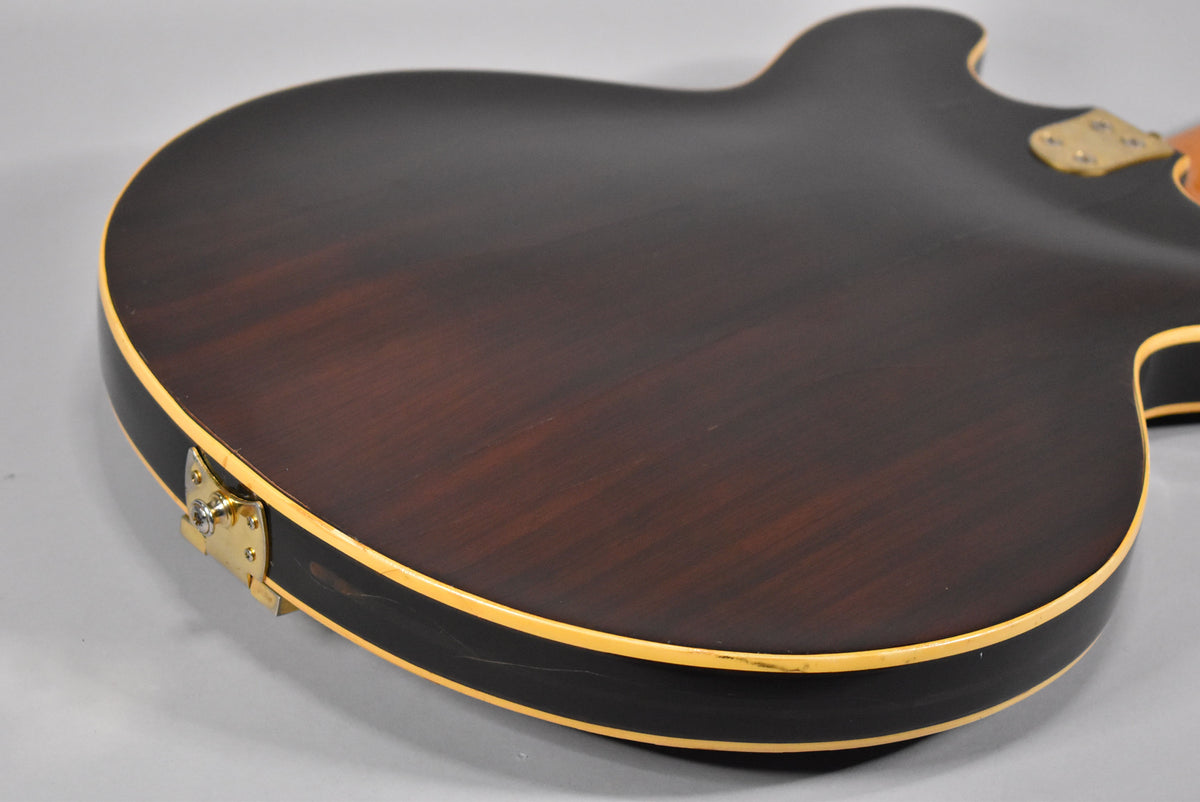 The guitar's dark walnut back and sides, with cream binding, show some wear and scratches, especially near the gold strap button.