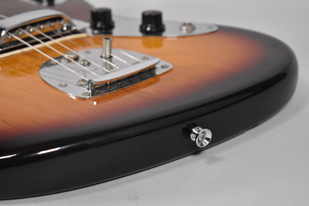Close-up of the lower bout of a 3-Tone Sunburst guitar, showing the chrome bridge, vibrato, and strap button, with some light wear.